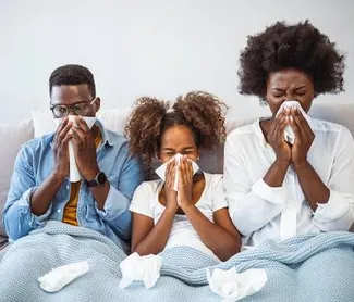 Family of three at home with matching cold and flu symptoms, each blowing their nose