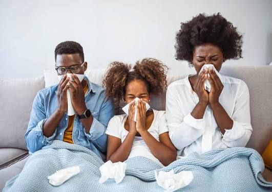 Family of three at home with matching cold and flu symptoms, each blowing their nose